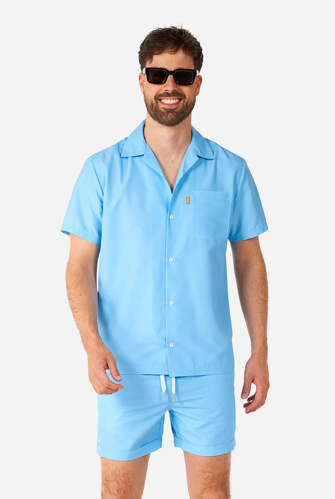 Man in lichtblauwe zomerset, bestaande uit shirt en korte broek