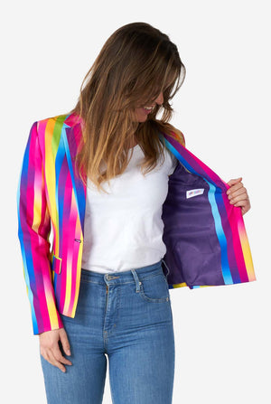 Afbeelding van een vrouw, gekleed in verticaal gestreepte regenboogkleurige damesblazer, wit overhemd en spijkerbroek. Ze houdt één kant van de blazer open, waardoor de paarse voering zichtbaar is.