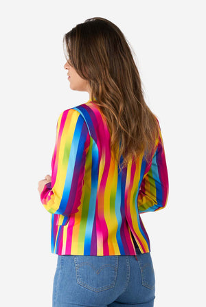 Afbeelding van een vrouw, gekleed in verticaal gestreepte regenboogkleurige damesblazer, wit overhemd en spijkerbroek. Ze houdt de zijkanten van de blazer vast. Uitzicht vanaf de achterkant.