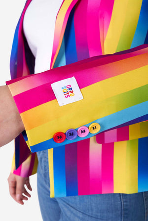 Close-up beeld van een vrouw, gekleed in verticaal gestreepte regenboogkleurige damesblazer, wit overhemd en spijkerbroek. Ze laat de mouw met gekleurde knopen zien.