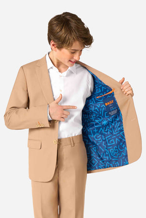 Tienerjongen draagt een stijlvol lichtbruin/beige pak met een wit overhemd en ziet er zelfverzekerd uit. Perfecte formele outfit voor speciale gelegenheden, bruiloften en feesten voor jongens. Houdt een kant van het jasje open.