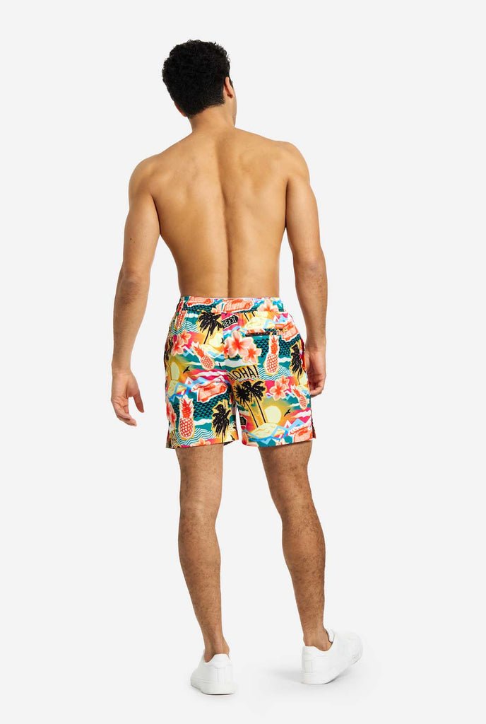 Man wearing swim trunks with tropical Hawaiian print, view from the back