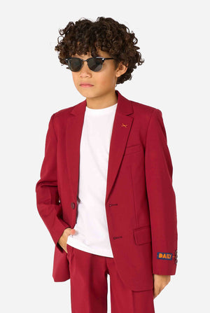 Een kind in een stijlvol bordeauxrood pak met een wit overhemd, dat er zelfverzekerd uitziet en draagt een zonnebril. De perfecte formele outfit voor speciale gelegenheden, bruiloften en feestjes voor jongens. Houd een hand in een broekzak.