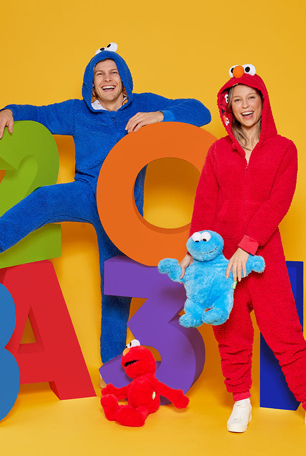 Twee mensen in kleurrijke Sesamstraat-onesies tegen een gele achtergrond