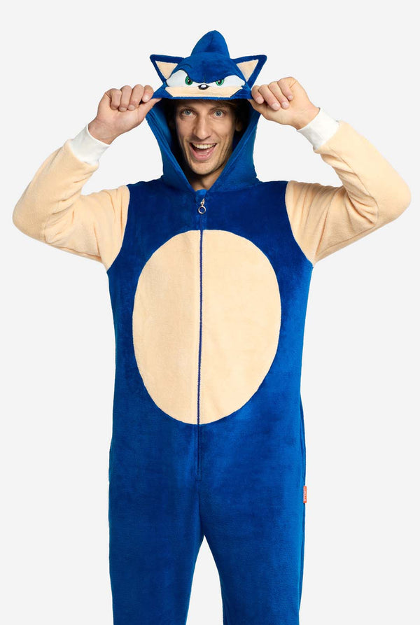 Een man draagt ​​een speelse blauw-beige Sonic the Hedgehog-onesie voor volwassenen van OppoSuits. De gezellige onesie heeft een ritssluiting aan de voorkant en een vaste capuchon die is ontworpen om op het iconische gezicht van Sonic te lijken, compleet met oren en een expressieve blik. De blauwe body van het pak contrasteert met een beige buik, wat de klassieke look van Sonic nabootst. Deze leuke, comfortabele en stijlvolle onesie is perfect voor loungen, themafeesten of cosplay-evenementen.
