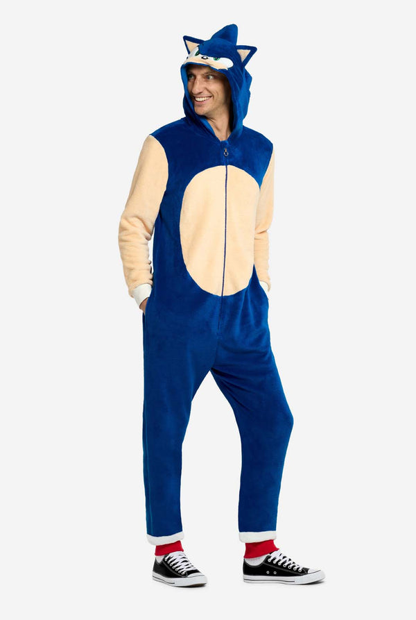 Een man draagt ​​een speelse blauw-beige Sonic the Hedgehog-onesie voor volwassenen van OppoSuits. De gezellige onesie heeft een ritssluiting aan de voorkant en een vaste capuchon die is ontworpen om op het iconische gezicht van Sonic te lijken, compleet met oren en een expressieve blik. De blauwe body van het pak contrasteert met een beige buik, wat de klassieke look van Sonic nabootst. 