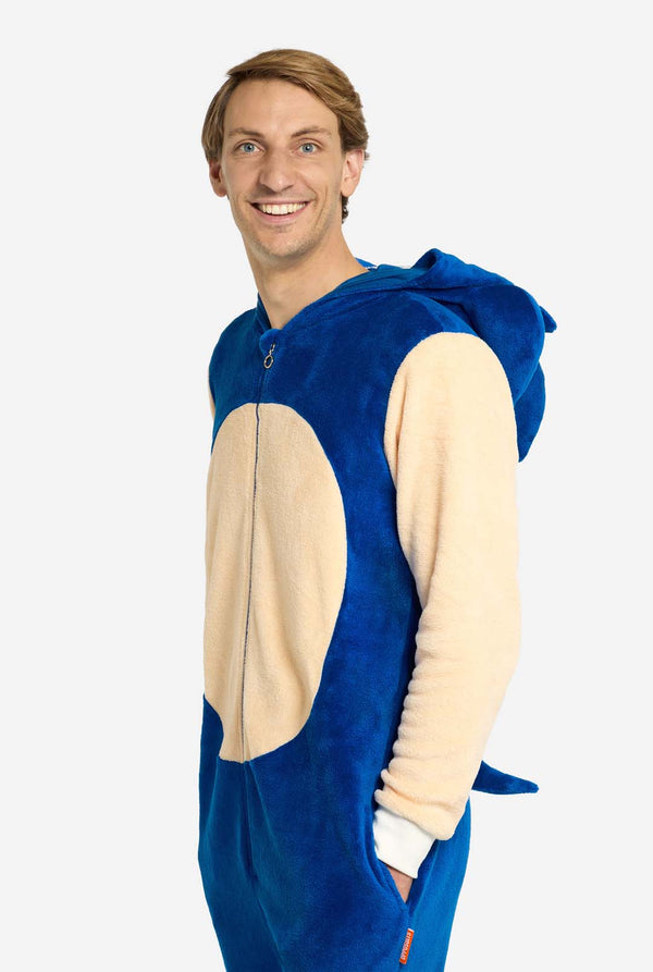Een man draagt ​​een speelse blauw-beige Sonic the Hedgehog-onesie voor volwassenen van OppoSuits. De gezellige onesie heeft een ritssluiting aan de voorkant en een vaste capuchon die is ontworpen om op het iconische gezicht van Sonic te lijken, compleet met oren en een expressieve blik. De blauwe body van het pak contrasteert met een beige buik, wat de klassieke look van Sonic nabootst. Zijwaarts staan ​​en in de camera kijken.