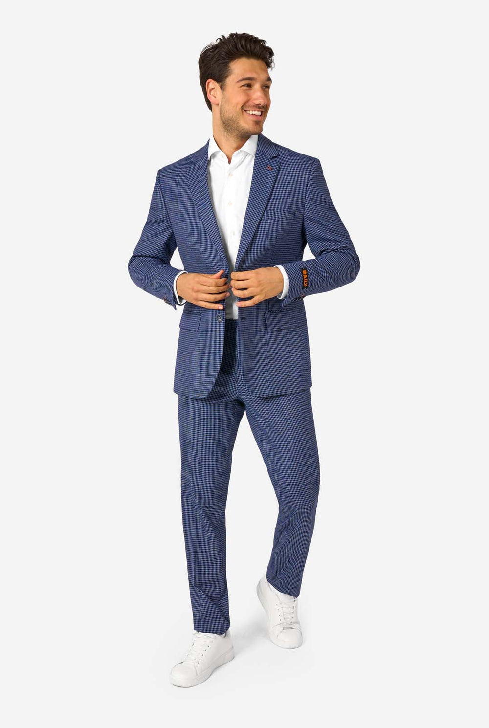 Een man draagt een marineblauw en blauw geruit pak met een wit overhemd. Het pak heeft een moderne pasvorm met twee knopen en klepzakken. Hij staat tegen een effen witte achtergrond.
