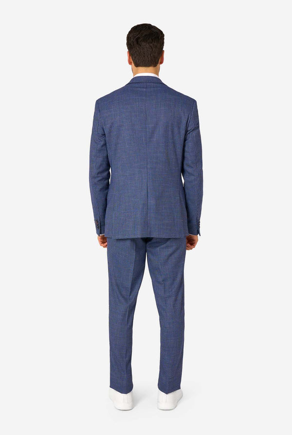 Een man draagt een marineblauw en blauw geruit pak met een wit overhemd. Het pak heeft een moderne pasvorm met twee knopen en klepzakken. Hij staat tegen een effen witte achtergrond. Zicht vanaf de achterkant