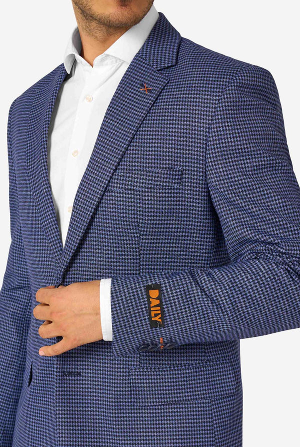Een man draagt een marineblauw en blauw geruit pak met een wit overhemd. Het pak heeft een moderne pasvorm met twee knopen en klepzakken. Hij staat tegen een effen witte achtergrond. Close up van de borst