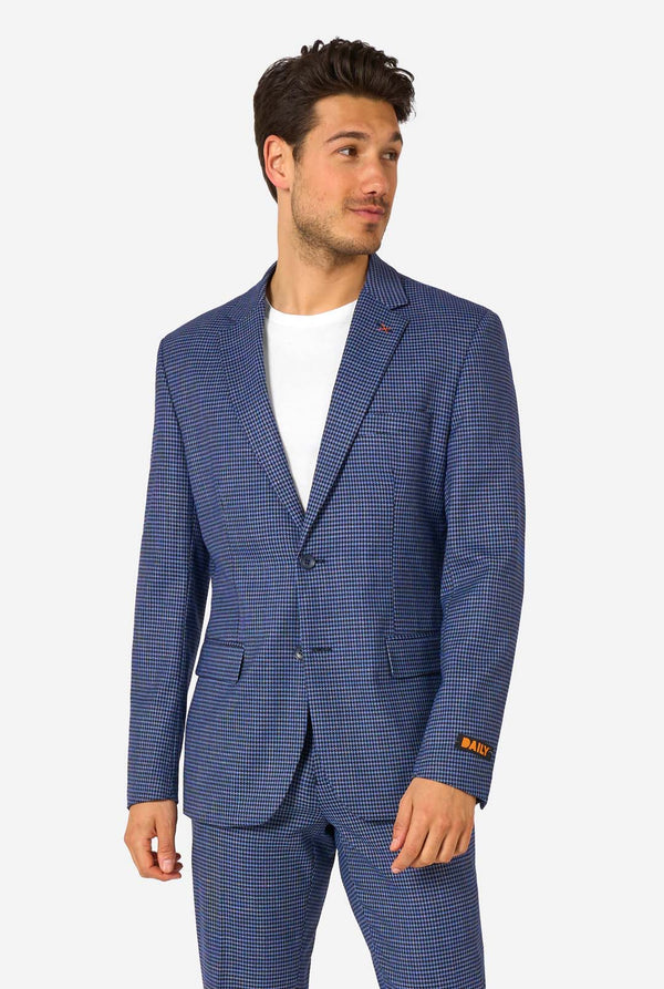 Een man draagt een marineblauw en blauw geruit pak met een wit overhemd. Het pak heeft een moderne pasvorm met twee knopen en klepzakken. Hij staat tegen een effen witte achtergrond.