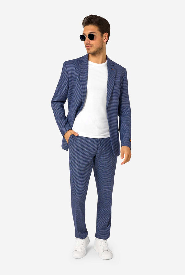 Een man draagt een marineblauw en blauw geruit pak met een wit overhemd. Het pak heeft een moderne pasvorm met twee knopen en klepzakken. Hij staat tegen een effen witte achtergrond. Volledig lichaam, draagt een zonnebril