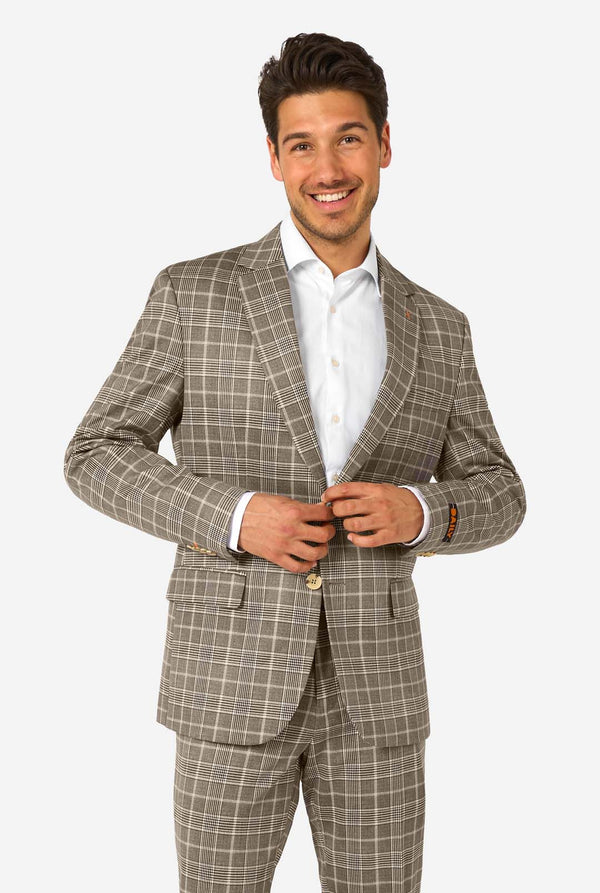 Een man draagt een bruin geruit pak met een wit overhemd. Het pak heeft een moderne pasvorm met twee knopen en klepzakken. Hij staat tegen een effen witte achtergrond.