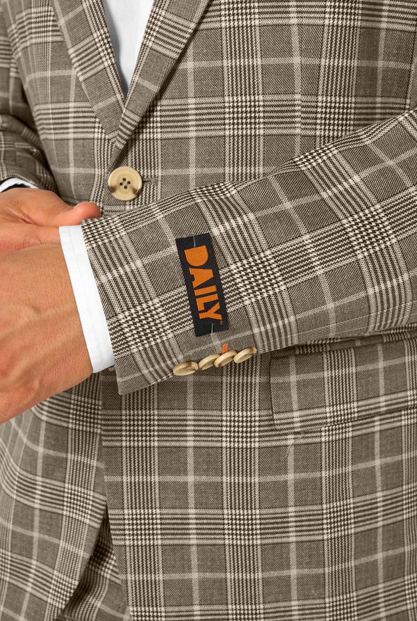 Een man draagt een bruin geruit pak met een wit overhemd. Het pak heeft een moderne pasvorm met twee knopen en klepzakken. Hij staat tegen een effen witte achtergrond. Close up van de mouwen