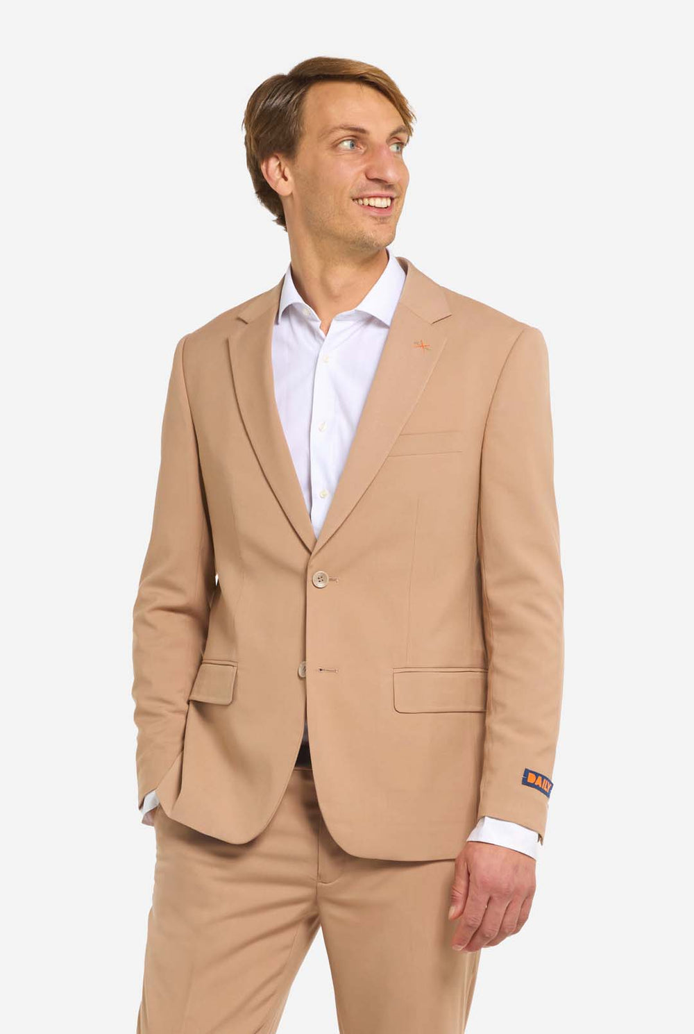 Afbeelding met lichtgrijze achtergrond en man die donker zand mannenpak en wit overhemd draagt. Pak bestaat uit blazer en broek. Kijkt naar de zijkant.