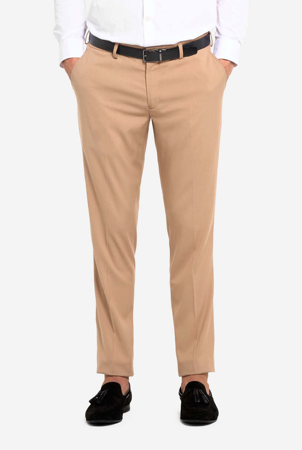 Afbeelding met lichtgrijze achtergrond en man die donker zand mannenpak en wit overhemd draagt. Pak bestaat uit blazer en broek. Gericht op de broek.