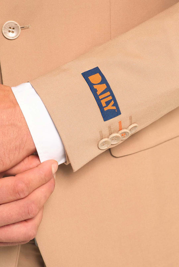 Afbeelding met lichtgrijze achtergrond en man die donker zand mannenpak en wit overhemd draagt. Pak bestaat uit blazer en broek. Gericht op de mouwen.