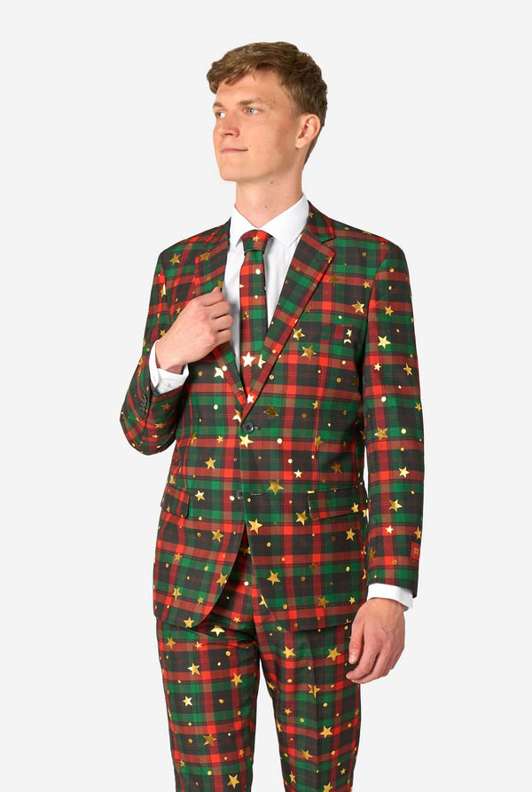 Man draagt een rood-groen tartan ruitpak met gouden sterren- en stipaccenten, en stelt zijn bijpassende stropdas recht.
