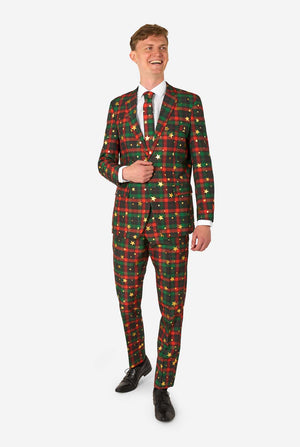 Man in een rood-groen tartan ruitpak met gouden sterren- en stipaccenten, glimlacht terwijl hij staat met één hand bij de jas¬knop.