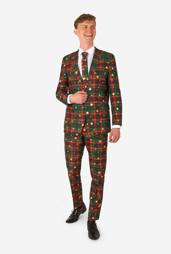 Man in een rood-groen tartan ruitpak met gouden sterren- en stipaccenten, glimlacht terwijl hij staat met één hand bij de jas¬knop.