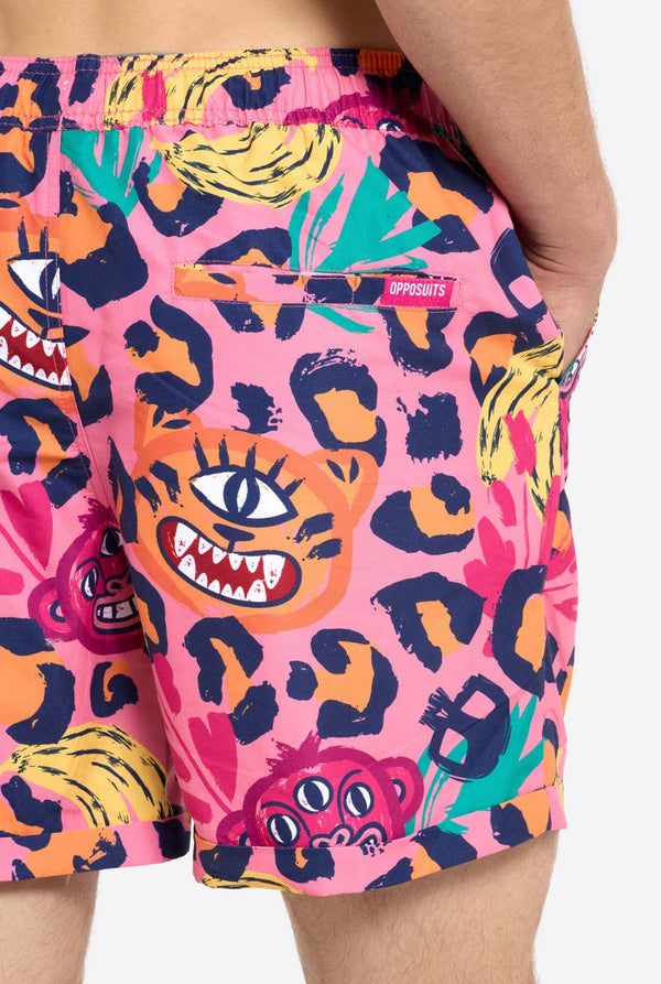 Een man die een levendige tweedelige zomeroutfit draagt ​​met een opvallende tropische print. Het overhemd met korte mouwen en de bijpassende shorts hebben een levendig ontwerp met neonroze, oranje en gele luipaardprints, bananen, groene palmbladeren en eigenzinnige cartoongezichten. De outfit is nonchalant gestyled met een groen T-shirt eronder en is perfect voor zomerfeestjes, vakanties of plezier bij het zwembad. Achterkant van korte close-up.