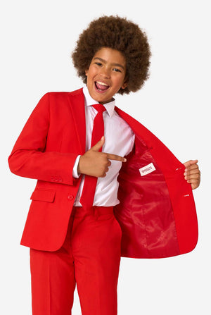 Kind draagt een rood pak met een wit overhemd en een rode stropdas op een witte achtergrond. Houdt zijn jasje open