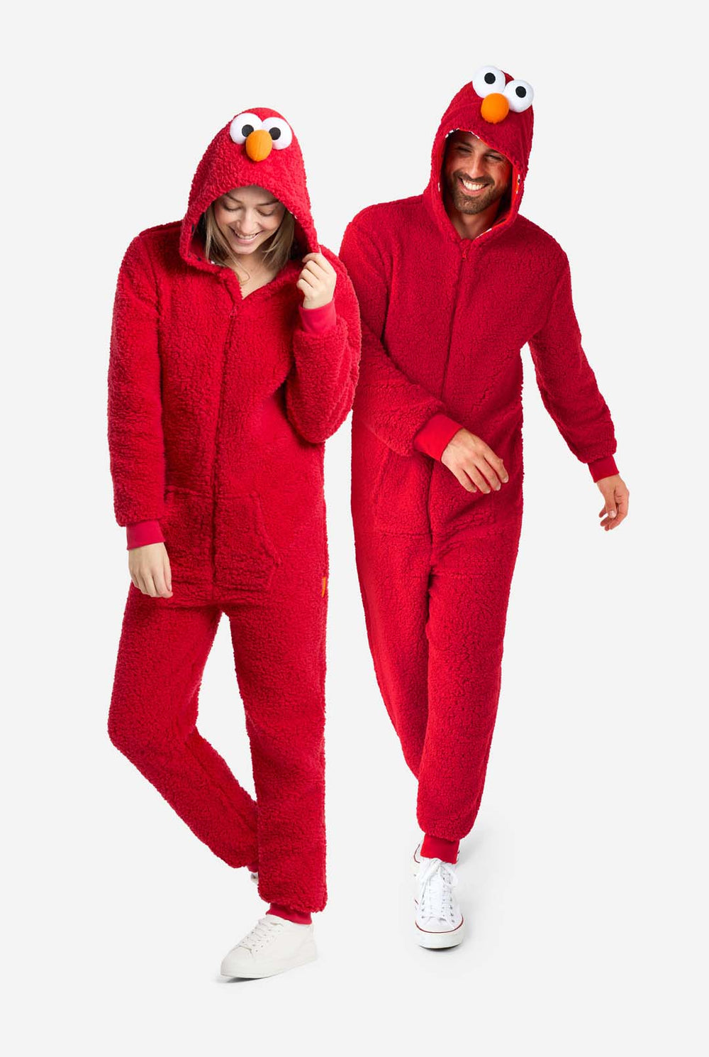 Een man en een vrouw zijn gekleed in een rode Elmo-onesie. Het algehele ontwerp imiteert de look van het Sesame Street-personage Elmo. De achtergrond is effen, waardoor de nadruk op het kostuum ligt.