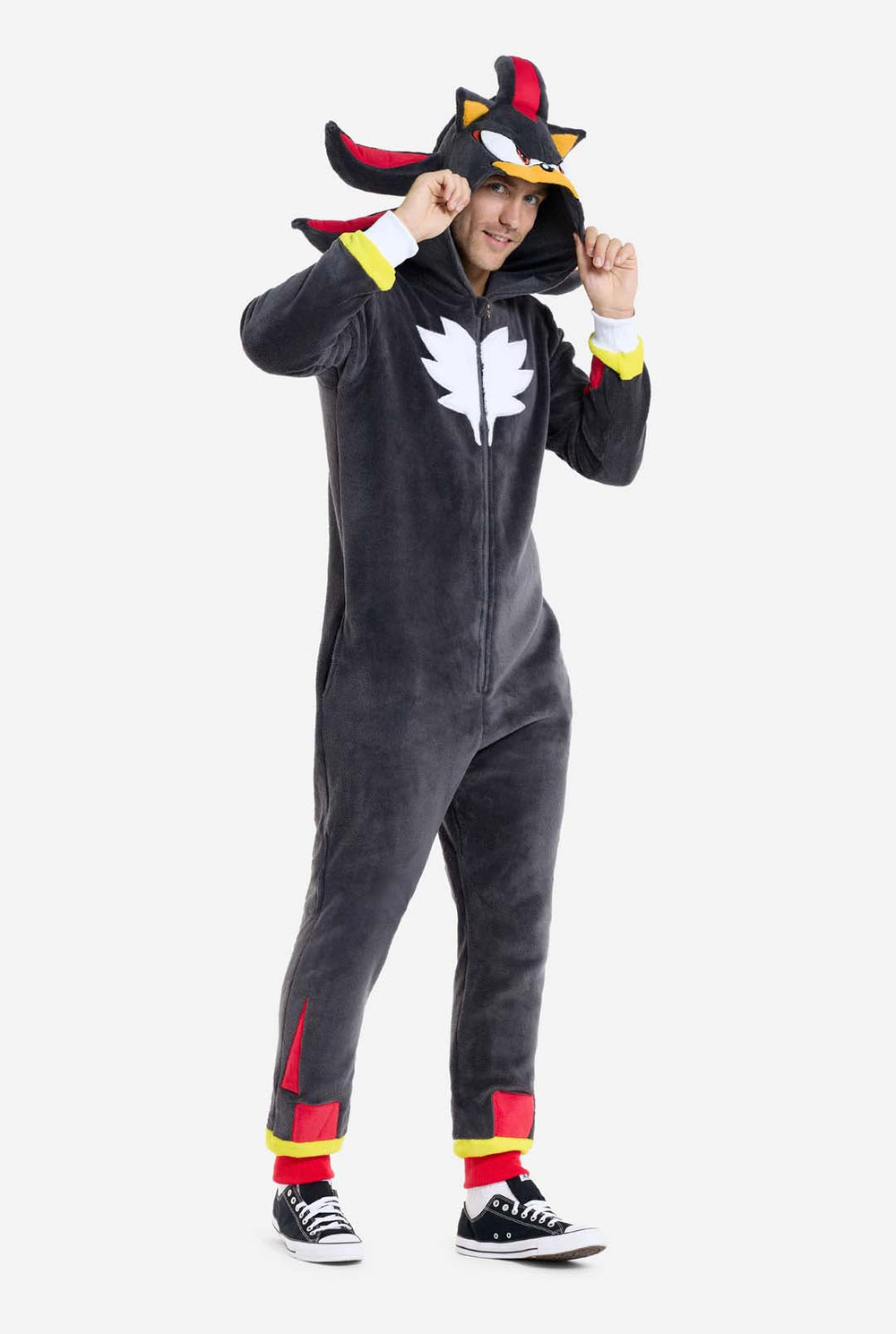 Een man draagt ​​een pluchen zwarte onesie, geïnspireerd op het populaire egelpersonage Shadow, met puntige rode en zwarte accenten op de capuchon, een wit embleem op de borst en gele details op de polsen. De onesie is gemaakt van zacht fleecemateriaal en biedt comfort en een speels ontwerp voor cosplay, loungen of thema-evenementen. De persoon glimlacht terwijl hij de capuchon aantrekt, waardoor het herkenbare gezicht en het opvallende ontwerp van het personage zichtbaar zijn.