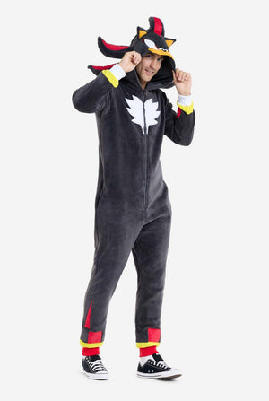 Een man met een pluchen zwarte onesie geïnspireerd op het populaire egelkarakter Shadow, met puntige rode en zwarte accenten op de capuchon, een wit embleem op de borst en gele polsdetails. De onesie is gemaakt van zacht fleecemateriaal en biedt comfort en een speels ontwerp voor cosplay, loungen of thema-evenementen. De persoon glimlacht terwijl hij de capuchon vasthoudt, wat het herkenbare gezicht en het opvallende ontwerp van het personage laat zien. Perfect voor fans van gaming of geanimeerde karakters.