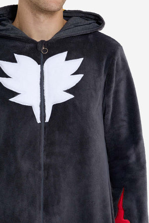 Een man met een pluchen zwarte onesie geïnspireerd op het populaire egelkarakter Shadow, met puntige rode en zwarte accenten op de capuchon, een wit embleem op de borst en gele polsdetails. De onesie is gemaakt van zacht fleecemateriaal en biedt comfort en een speels ontwerp voor cosplay, loungen of thema-evenementen. Borst close-up. Perfect voor fans van gaming of geanimeerde karakters.