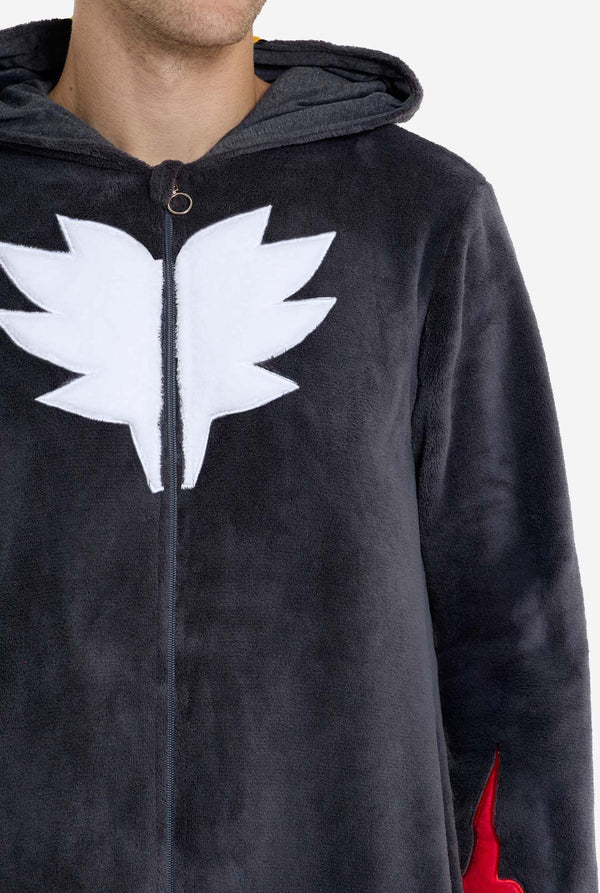 Een man met een pluchen zwarte onesie geïnspireerd op het populaire egelkarakter Shadow, met puntige rode en zwarte accenten op de capuchon, een wit embleem op de borst en gele polsdetails. De onesie is gemaakt van zacht fleecemateriaal en biedt comfort en een speels ontwerp voor cosplay, loungen of thema-evenementen. Borst close-up. Perfect voor fans van gaming of geanimeerde karakters.