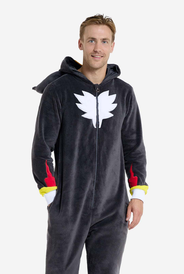 Een man met een pluchen zwarte onesie geïnspireerd op het populaire egelkarakter Shadow, met puntige rode en zwarte accenten op de capuchon, een wit embleem op de borst en gele polsdetails. De onesie is gemaakt van zacht fleecemateriaal en biedt comfort en een speels ontwerp voor cosplay, loungen of thema-evenementen. De persoon glimlacht terwijl de kap op zijn rug ligt. Perfect voor fans van gaming of geanimeerde karakters.