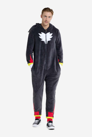 Een man met een pluchen zwarte onesie geïnspireerd op het populaire egelkarakter Shadow, met puntige rode en zwarte accenten op de capuchon, een wit embleem op de borst en gele polsdetails. De onesie is gemaakt van zacht fleecemateriaal en biedt comfort en een speels ontwerp voor cosplay, loungen of thema-evenementen. De persoon glimlacht terwijl de kap op zijn rug ligt. Perfect voor fans van gaming of geanimeerde karakters. Volledig lichaamsbeeld.