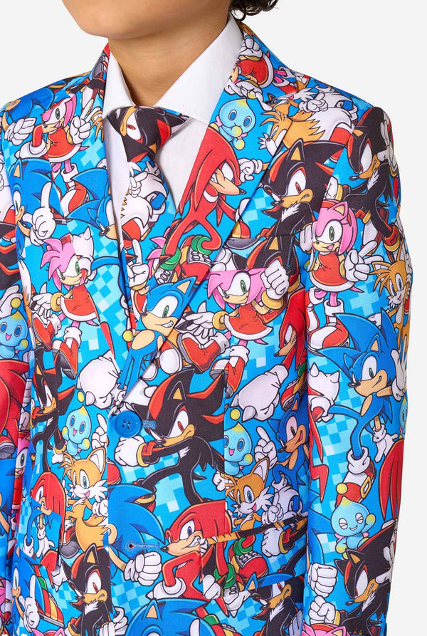 Jonge jongen draagt een levendig Sonic-tienerpak met kleurrijke opdrukken van Sonic the Hedgehog-personages zoals Sonic, Knuckles, Tails en Amy, gecombineerd met een bijpassende stropdas en wit overhemd. Gefocust op de borst