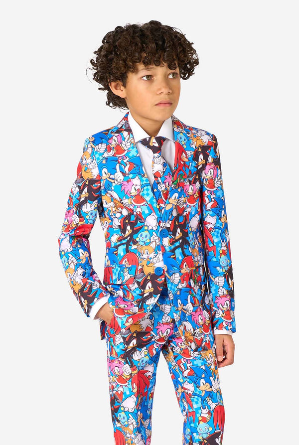 Jonge jongen draagt een levendig Sonic-tienerpak met kleurrijke opdrukken van Sonic the Hedgehog-personages zoals Sonic, Knuckles, Tails en Amy, gecombineerd met een bijpassende stropdas en wit overhemd. Hij kijkt naar de zijkant