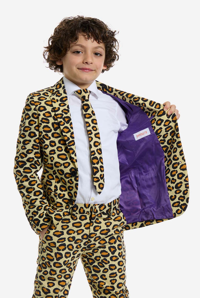 Op deze afbeelding draagt ​​een kind een jongenspak met all-over panterprint en een wit shirt. Het pak is beige met bruine en zwarte gevlekte panterprint. Pakken bestaan ​​uit een jasje, broek en clip-on stropdas. Een kant van jasje open.
