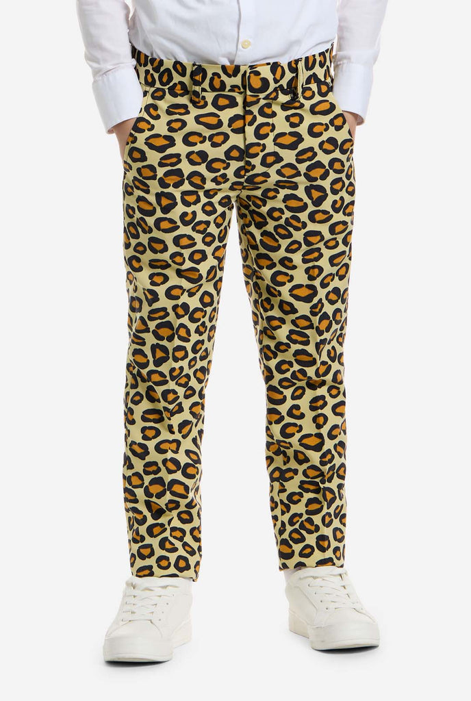 Op deze afbeelding draagt ​​een kind een jongenspak met all-over panterprint en een wit shirt. Het pak is beige met bruine en zwarte gevlekte panterprint. Pakken bestaan ​​uit een jasje, broek en clip-on stropdas. Close up broek.