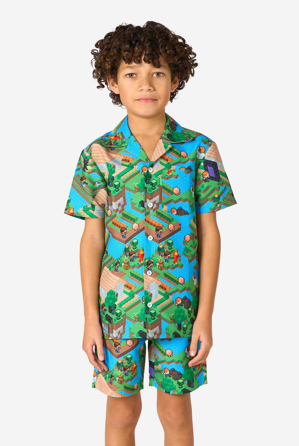Een jonge jongen draagt een kleurrijke zomeroutfit met een Minecraft Overworld print, met pixelachtige landschappen, personages en elementen uit het iconische spel. Het shirt met korte mouwen en de bijpassende shorts benadrukken een levendig ontwerp geïnspireerd door het Minecraft-universum.