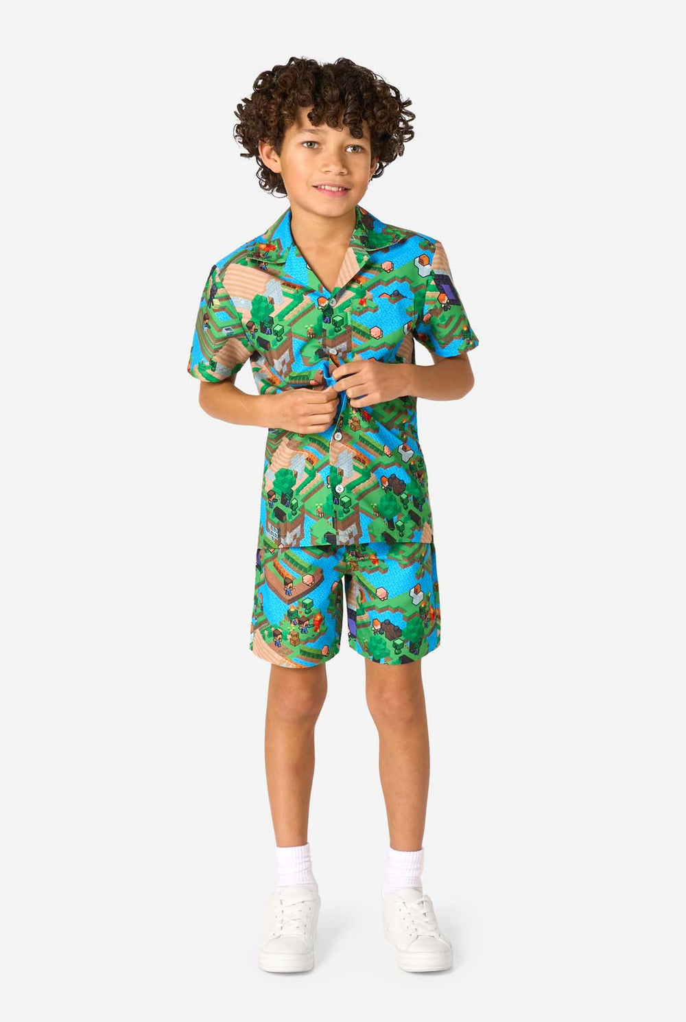 Een jonge jongen draagt een kleurrijke zomeroutfit met een Minecraft Overworld print, met pixelachtige landschappen, personages en elementen uit het iconische spel. Het shirt met korte mouwen en de bijpassende shorts benadrukken een levendig ontwerp geïnspireerd door het Minecraft-universum.