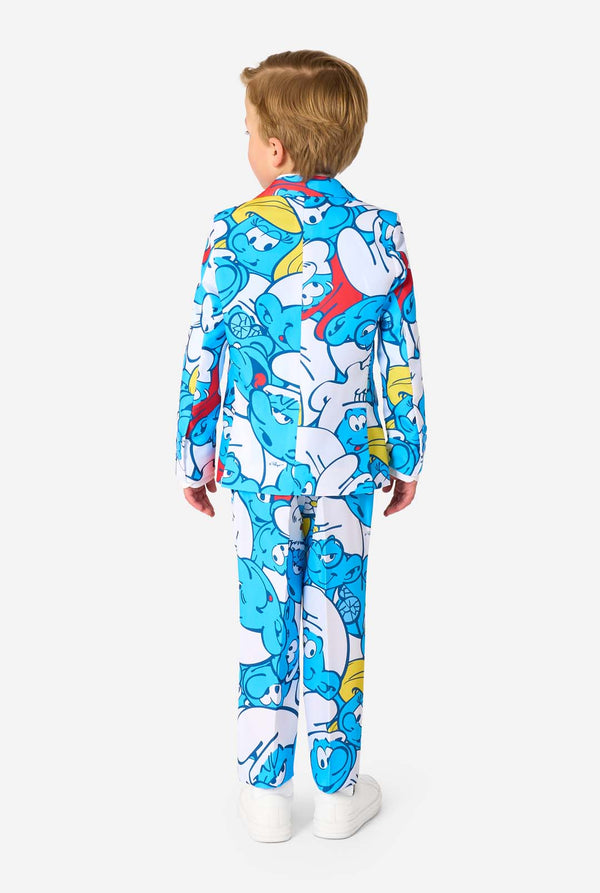 Een jongetje draagt ​​een kleurrijk Smurfenpak met daarop opvallende blauwe cartoonfiguurprints, inclusief jasje, broek en bijpassende stropdas, en lacht tegen een effen witte achtergrond. Gezien vanaf de achterkant.