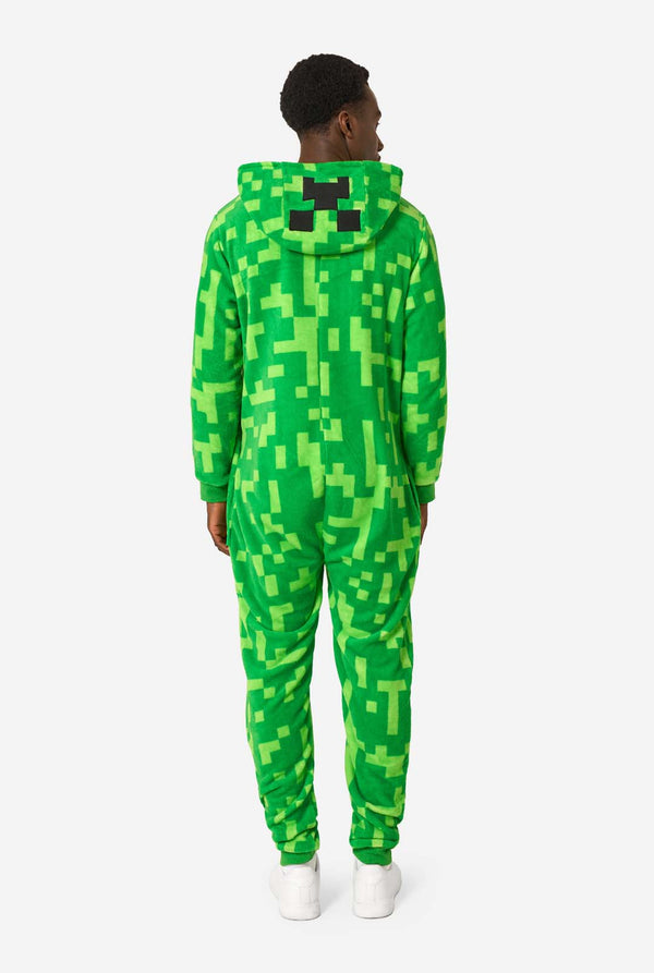 Een man die een groene, pixelachtige onesie draagt, ontworpen om op het Minecraft Creeper-personage te lijken. De onesie heeft een capuchon met het iconische zwarte pixelgezicht van de Creeper. De man heeft de capuchon op zijn rug. Uitzicht vanaf de achterkant.