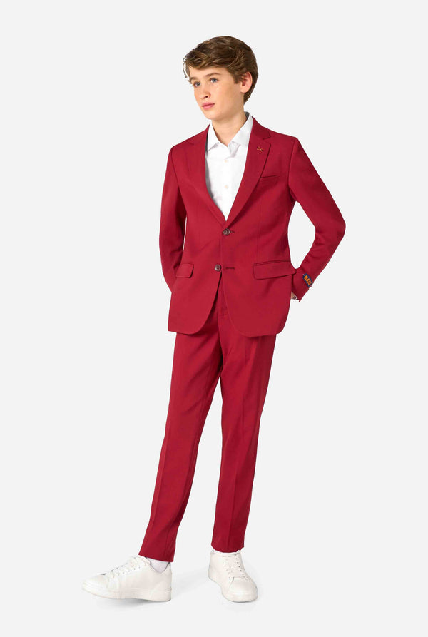 Tienerjongen draagt ​​een stijlvol bordeauxrood pak met een wit overhemd en ziet er zelfverzekerd uit. Perfecte formele outfit voor speciale gelegenheden, bruiloften en feesten voor jongens. Volledig lichaam foto.