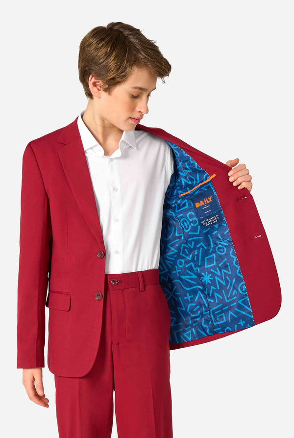 Tienerjongen draagt ​​een stijlvol bordeauxrood pak met een wit overhemd en ziet er zelfverzekerd uit. Perfecte formele outfit voor speciale gelegenheden, bruiloften en feesten voor jongens. Houdt een kant van het jasje open.