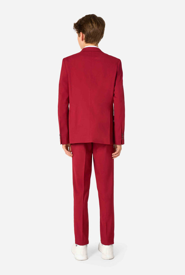 Tienerjongen draagt ​​een stijlvol bordeauxrood pak met een wit overhemd. Perfecte formele outfit voor speciale gelegenheden, bruiloften en feesten voor jongens. Zicht vanaf de achterkant.