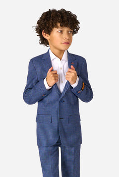 Een jongen, gekleed in een marineblauw en blauw geruit pak met een wit overhemd. Het pak heeft een moderne pasvorm met twee knopen en klepzakken. Hij staat tegen een effen witte achtergrond.