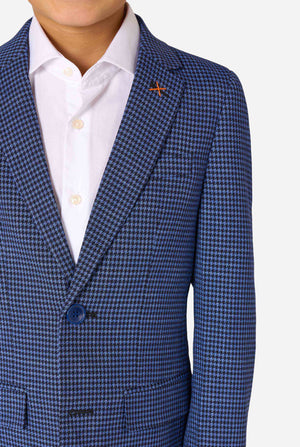 Een jongen, gekleed in een marineblauw en blauw geruit pak met een wit overhemd. Het pak heeft een moderne pasvorm met twee knopen en klepzakken. Hij staat tegen een effen witte achtergrond. Close-up van de borst