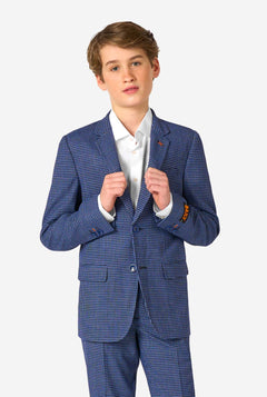 Een tienerjongen, gekleed in een marineblauw en blauw geruit pak met een wit overhemd. Het pak heeft een moderne pasvorm met twee knopen en klepzakken. Hij staat tegen een effen witte achtergrond.