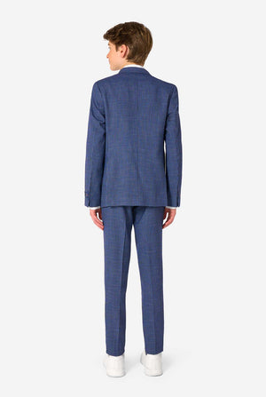 Een tienerjongen, gekleed in een marineblauw en blauw geruit pak met een wit overhemd. Het pak heeft een moderne pasvorm met twee knopen en klepzakken. Hij staat tegen een effen witte achtergrond. Zicht vanaf de achterkant