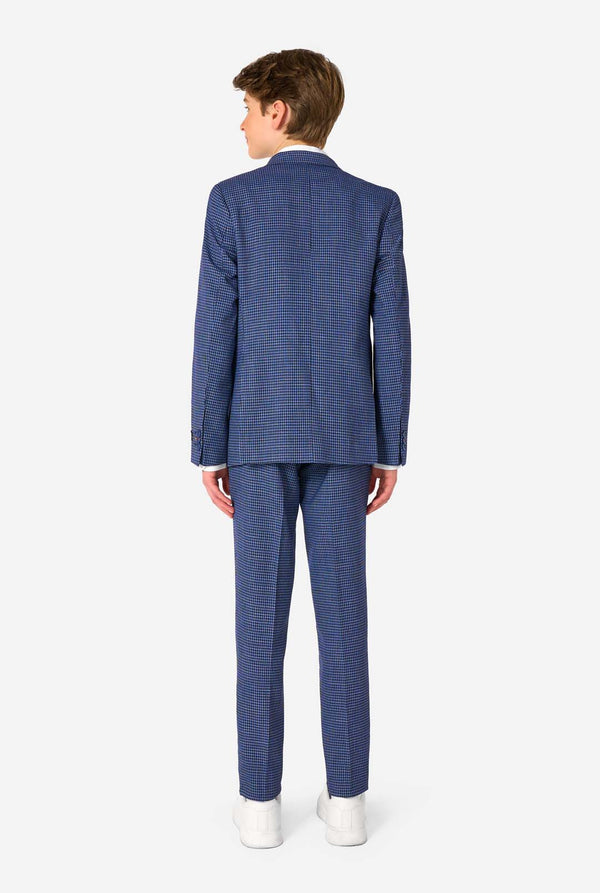 Een tienerjongen, gekleed in een marineblauw en blauw geruit pak met een wit overhemd. Het pak heeft een moderne pasvorm met twee knopen en klepzakken. Hij staat tegen een effen witte achtergrond. Zicht vanaf de achterkant