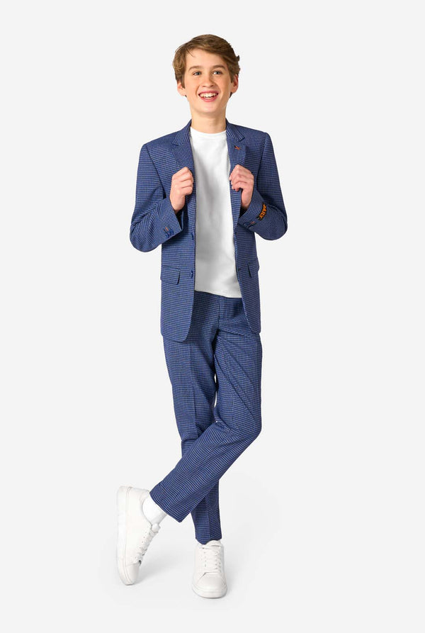Een tienerjongen, gekleed in een marineblauw en blauw geruit pak met een wit overhemd. Het pak heeft een moderne pasvorm met twee knopen en klepzakken. Hij staat tegen een effen witte achtergrond. Volledig lichaam